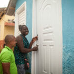 People unlocking a door to a blue house.