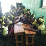 Smiling girls in school uniforms around a wooden table.