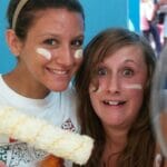 Two friends smiling with painted faces indoors.