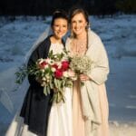 Two smiling women with bouquets in snowy setting.