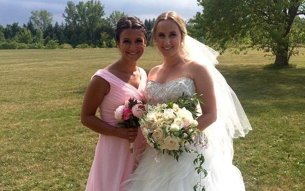 Bride and bridesmaid holding bouquets in a field.