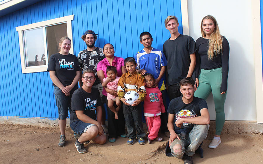 Group of people smiling in front of blue building.