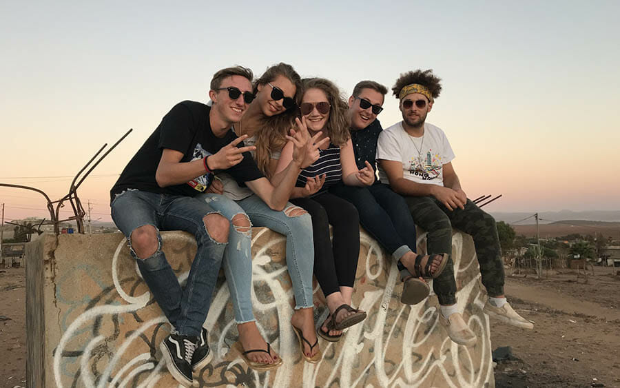 Friends sitting on graffiti wall at sunset.