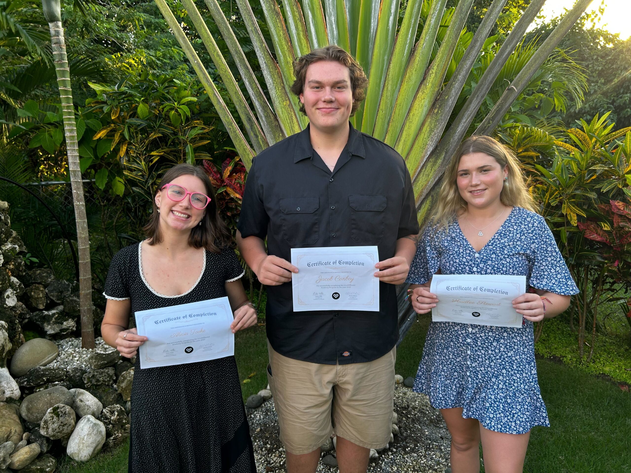 Three people holding completion certificates outside.