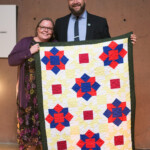 Two people holding colorful quilt display.