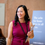 Woman in pink dress holding a clipboard, smiling.
