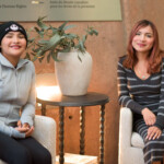Two women sitting and smiling indoors.