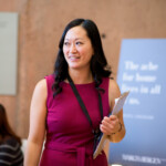 Woman in pink dress holding a clipboard, smiling.