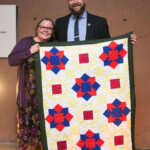 Two people holding colorful quilt display.